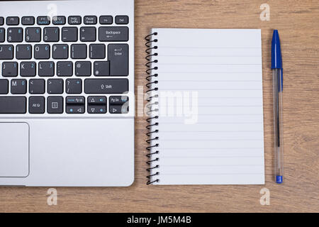 blank notepad with blue pen next to an open laptop Stock Photo