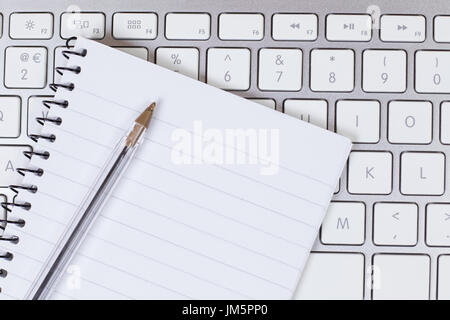 Business communication or learning concept with a blank notebook and ballpoint pen lying on the keyboard of an open laptop in a close up view Stock Photo