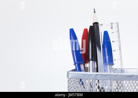Metal mesh desk tidy with several ballpoint pens, a pencil and ruler isolated on a white background with copy space in a concept of learning, teaching Stock Photo