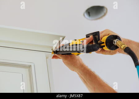 Carpenter brad using nail gun to Crown Moulding on kitchen cabinets framing trim, with the warning label that all power tools have on them shown illus Stock Photo