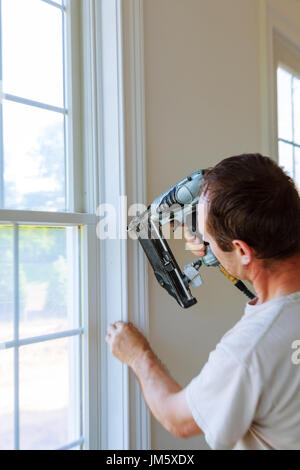 Carpenter using nail gun to moldings on windows, framing trim, with the warning that all power tools have on them shown illustrating safety concept Stock Photo