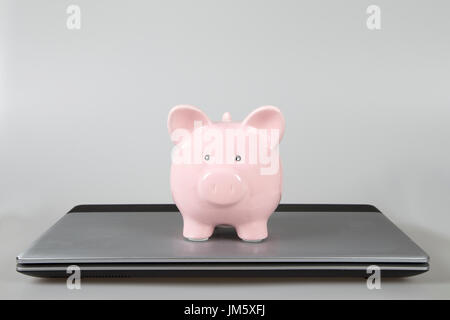 Pink piggy bank sitting on top of closed laptop Stock Photo