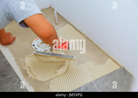 Stylish trendy white ceramic tile with a chamfer on the Tiler hands in the process of laying white rectangular tiles on bathroom wall. Repair of apart Stock Photo