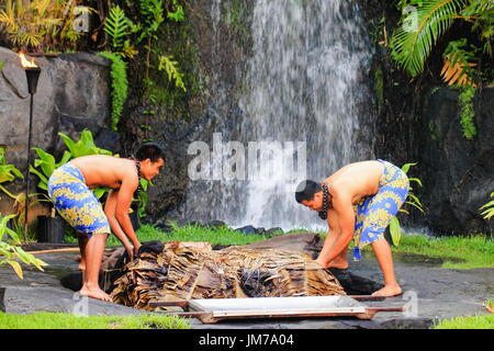 Honolulu, Hawaii - May 27, 2016: Two young Hawaiian men at the Polynesian Cultural Center uplift a pig cooked in the traditional style Kalua utilizing Stock Photo