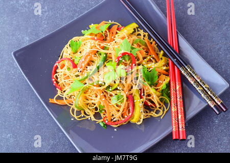 A grey ceramic plate with noodles and vegetables on a grey abstract background. Asian food. Healthy eating concept Stock Photo