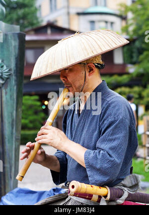 KYOTO, JAPAN - July 24, 2017: A busker wearing traditional Japanese clothes and a straw hat plays the Japanese shakuhachi for passersby in Maruyama Pa Stock Photo