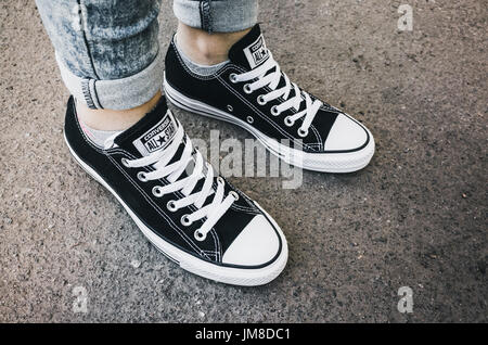 Saint-Petersburg, Russia - May 30, 2017: Teenager feet in a pair of black canvas Chuck Taylor All-Stars casual shoes stand on asphalt road