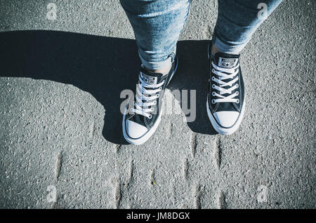 Saint-Petersburg, Russia - May 30, 2017: Teenager feet in a pair of black canvas Chuck Taylor All-Stars casual shoes stand on urban road