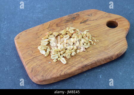 Crushed peanuts on a olive wood cutting board on a blue abstract background. Step by step cooking.. Stock Photo