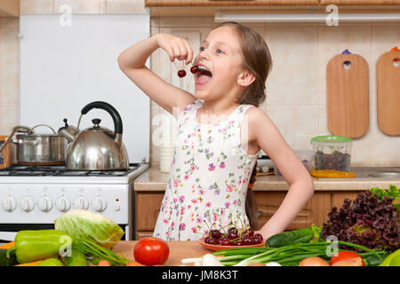 child girl eat cherries, fruits and vegetables in home kitchen interior, healthy food concept Stock Photo