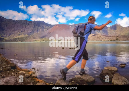 Girl jumping over stones in the water filled caldera of the Gunung Rinjani volcano in Lombok island, Indonesia Stock Photo