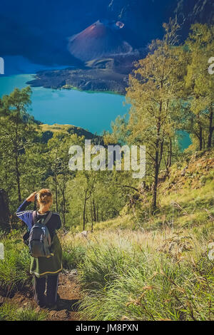 Caucasian girl with small backpack photographing the crater and cone of the Gunung Rinjani volcano, Lombok Stock Photo