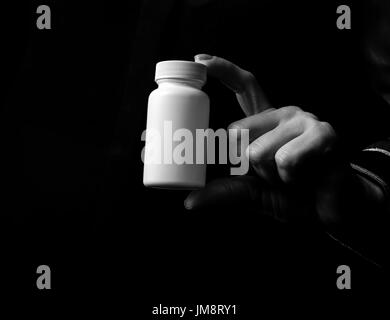 Black Mania. woman hand isolated on black showing bottle of medicine Stock Photo