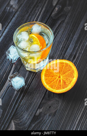 Cocktail with ice cubes and orange slice in a glass on dark wooden table Stock Photo