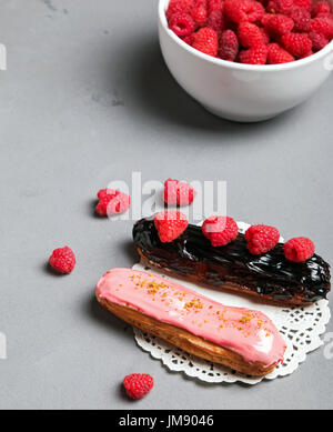 Delicious eclairs with glaze and fresh raspberries for decorating close-up Stock Photo