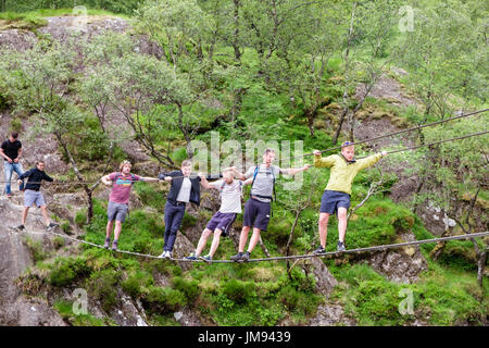 Six men messing about swinging on Steall wire bridge crossing Water of Nevis river. Glen Nevis, Fort Willaim, Highland, Scotland, UK, Britain Stock Photo