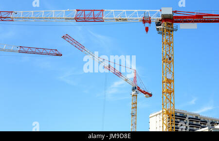 Low angle view of three tower cranes on a construction site with blue sky. Stock Photo