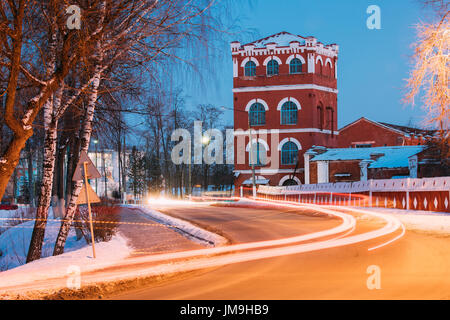 Dobrush, Gomel Region, Belarus. Old Paper Factory Tower At Winter Evening Or Night. Historical Heritage. Lunacharsky Avenue. Traffic Lights Trails On 