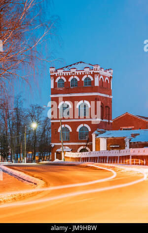 Dobrush, Gomel Region, Belarus. Old Paper Factory Tower At Winter Evening Or Night. Historical Heritage. Lunacharsky Avenue. Traffic Lights Trails On 