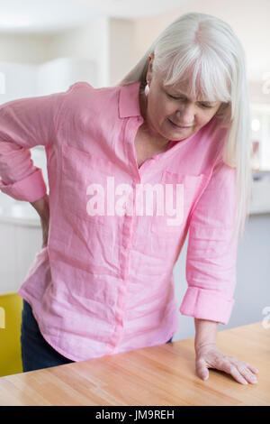 Senior Woman Suffering From Backache Whilst Getting Out Of Chair At Home Stock Photo