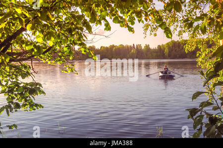 A young guy rides a boat on a lake during sunset. Man rowing in golden hour Stock Photo