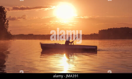 A young guy rides a boat on a lake during a golden sunset. Image of silhouette, sunset. Man rowing a boat in backlight of the sun. Contre-jour, backli Stock Photo