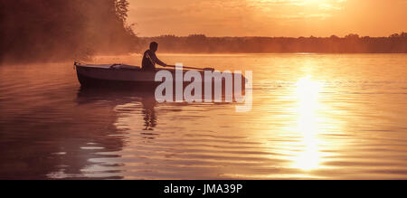 A young guy rides a boat on a lake during a golden sunset. Image of silhouette, sunset. Man rowing a boat in backlight of the sun. Contre-jour, backli Stock Photo