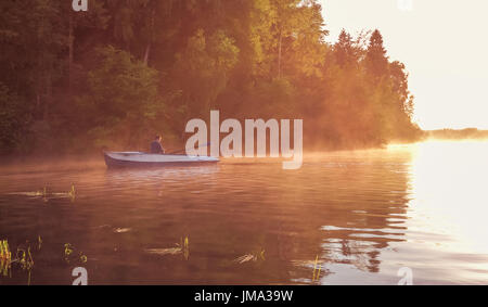 A young guy rides a boat on a lake during a golden sunset. Man rowing a boat in backlight of the sun. Unity with nature concept Stock Photo