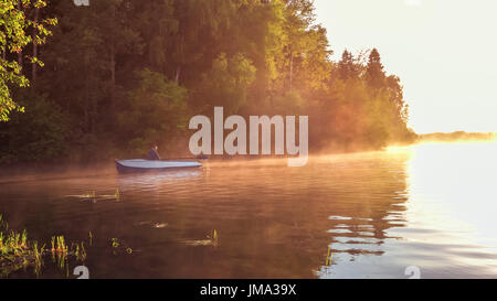 A young guy rides a boat on a lake during a golden sunset. Man rowing a boat in backlight of the sun. Unity with nature concept Stock Photo