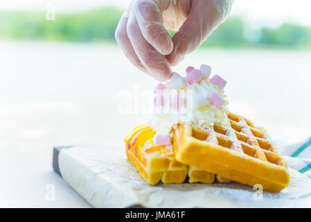 Close up hand adds marshmallows on top of belgian waffles with mango and cream Stock Photo