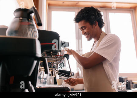 Professional barista holding cup on the coffee machine. Young man making coffee with an espresso coffee machine at cafe. Stock Photo