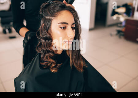 Close up of young woman at the salon getting her hair styled. Hair stylist turning straight hair into curly. Stock Photo