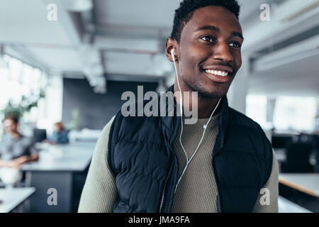 Male executive listening to music with earphones while standing in office. African young man listening music in design office. Stock Photo