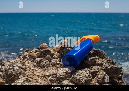 Sun cream sunscreen closeup laying on the beach rocks with dreamy sea and blue sky in the background during summer for tanning against sunburns Stock Photo