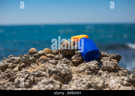 Sun cream sunscreen for tan laying on the heavenly summertime beach rocks with blue sea and blue sky in the background during summer for tanning again Stock Photo