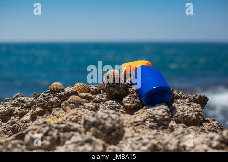 Sun cream sunscreen for tan laying on beach rocks on a sunny day with blue sea and blue sky in the background during summer for tanning against sunbur Stock Photo