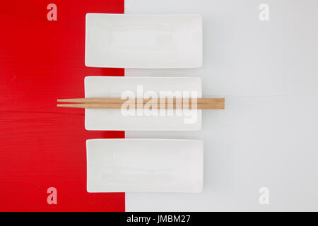 Empty ceramic bowls and bamboo chopsticks for sushi food on the red and white wooden table Stock Photo