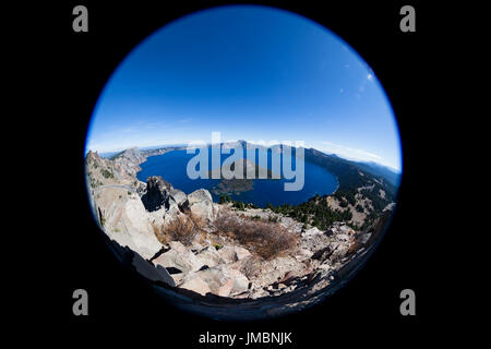Crater Lake in Oregon as seen through a fish eye lens showing the deep blue water, surrounding rock and mountains and a clear blue sky.