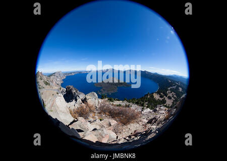 Crater Lake in Oregon as seen through a fish eye lens showing the deep blue water, surrounding rock and mountains and a clear blue sky.