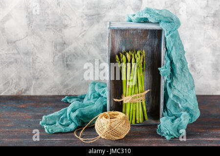 Raw asparagus, tangle of rope in wooden box on light background Stock Photo