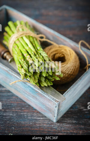 Raw asparagus, tangle of rope and knife in wooden box on dark wooden background Stock Photo
