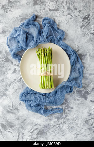 Bundle of raw asparagus on plate on light background. Top view Stock Photo