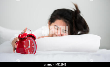 Asian women wake up from sleep. her hands hold at the clock And trying to turn off the alarm clock in the morning on the weekend in Relax and weekend  Stock Photo