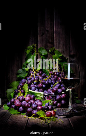 Fresh red grapes bunch lying on leaves on an old wooden table. Photographed with light painting technique Stock Photo