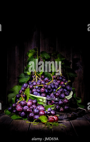 Fresh red grapes bunch lying on leaves on an old wooden table. Photographed with light painting technique Stock Photo