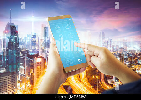 Smart remote home control system apps on a hand phone with double exposure effect futuristic city background . Stock Photo