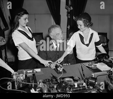 U.S. President Franklin Roosevelt with Two Camp Fire Girls Pressing Telegraph Key to Light Crossed Logs and Flame Lamp in Organization's New National Headquarters in New York City, Washington DC, USA, Harris & Ewing, March 1939 Stock Photo