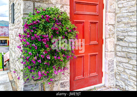 Purple pink magenta calibrachoa or petunia flowers hanging in basket by church with red door Stock Photo