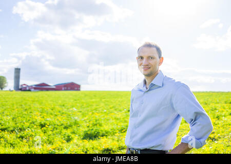 Young man standing in vast, open summer countryside field by red building Stock Photo