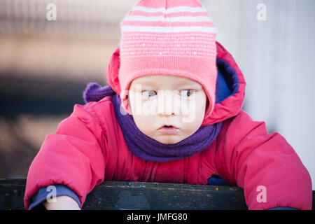 brown eyed girl child is standing on the fence looking left with red jumper Stock Photo